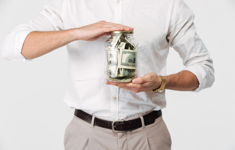 Person holding a glass jar filled with cash, representing saving money for a big purchase goal.