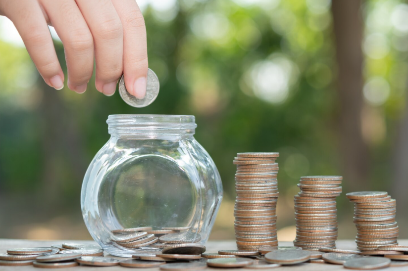 Hand adding a coin to a savings jar showing how small financial wins build momentum over time.