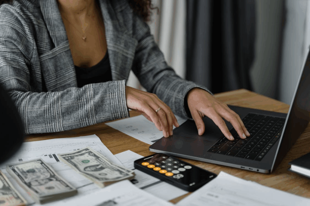 Person reviewing bills, cash, and budget on a laptop during a weekly money routine.